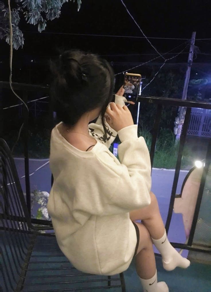 Gái trẻ xinh đẹp mặc áo sweatshirt trắng ngồi trên ghế ban công