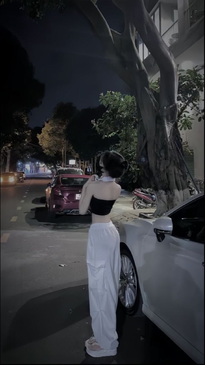 Gái xinh mặc áo crop top đen và quần trắng bên xe hơi