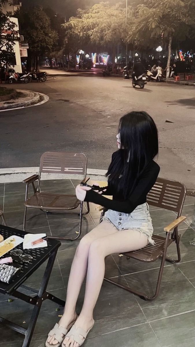 Gái xinh mặc áo dài tay đen và quần shorts ngồi ghế
