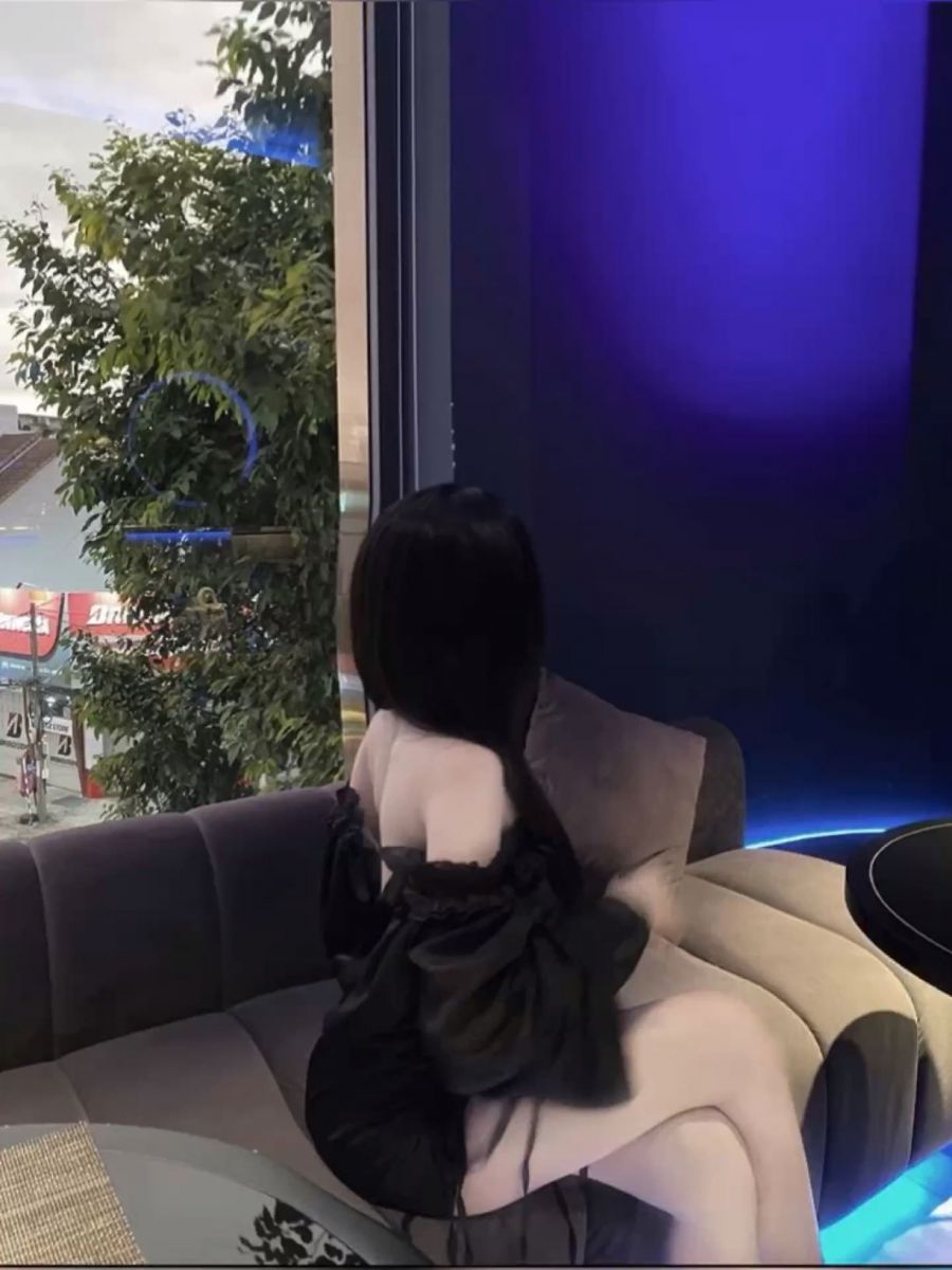 Gái xinh mặc áo đen ngồi trên sofa trong quán cà phê sang trọng