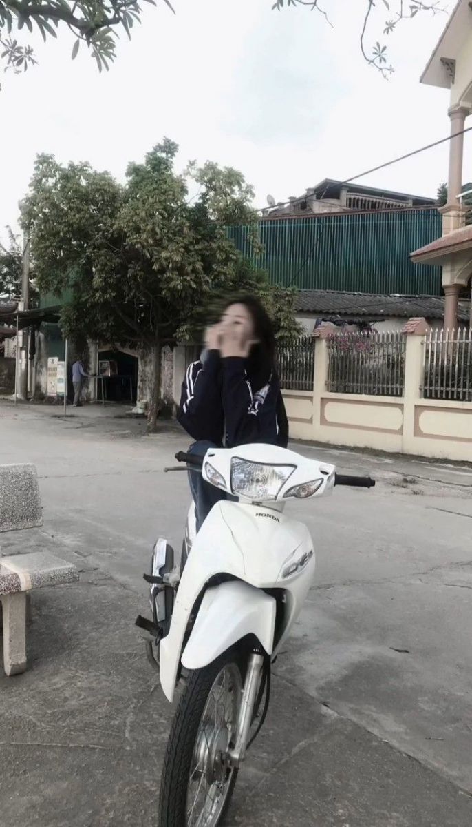 Gái xinh mặc áo khoác đen bên xe máy trắng
