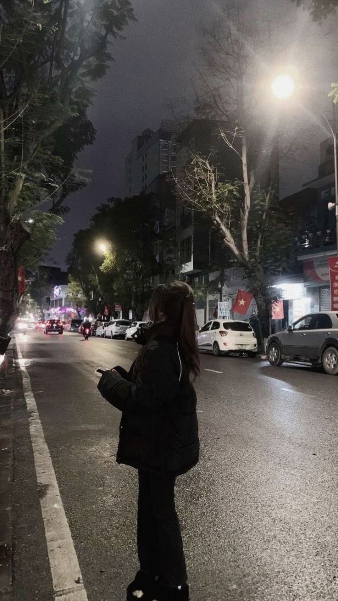 Gái xinh mặc áo khoác đen và quần tối giữa phố đêm