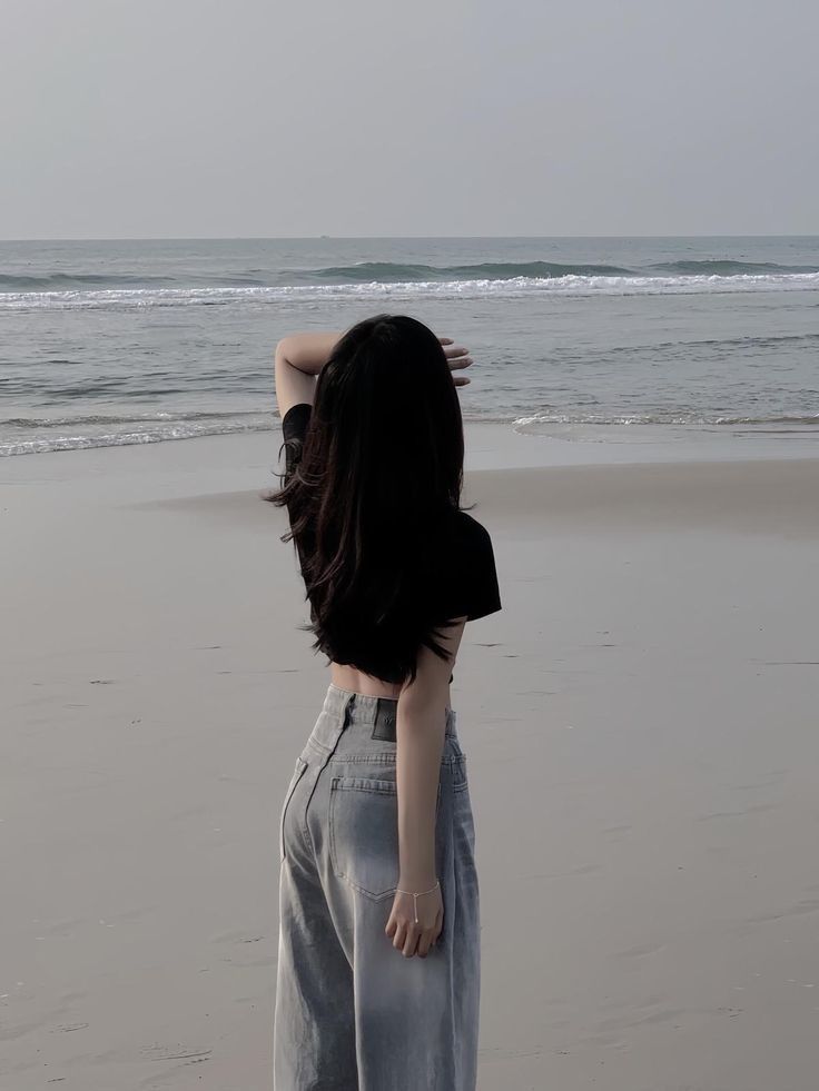 Gái xinh mặc áo thun đen và quần jeans rông bên bãi biển