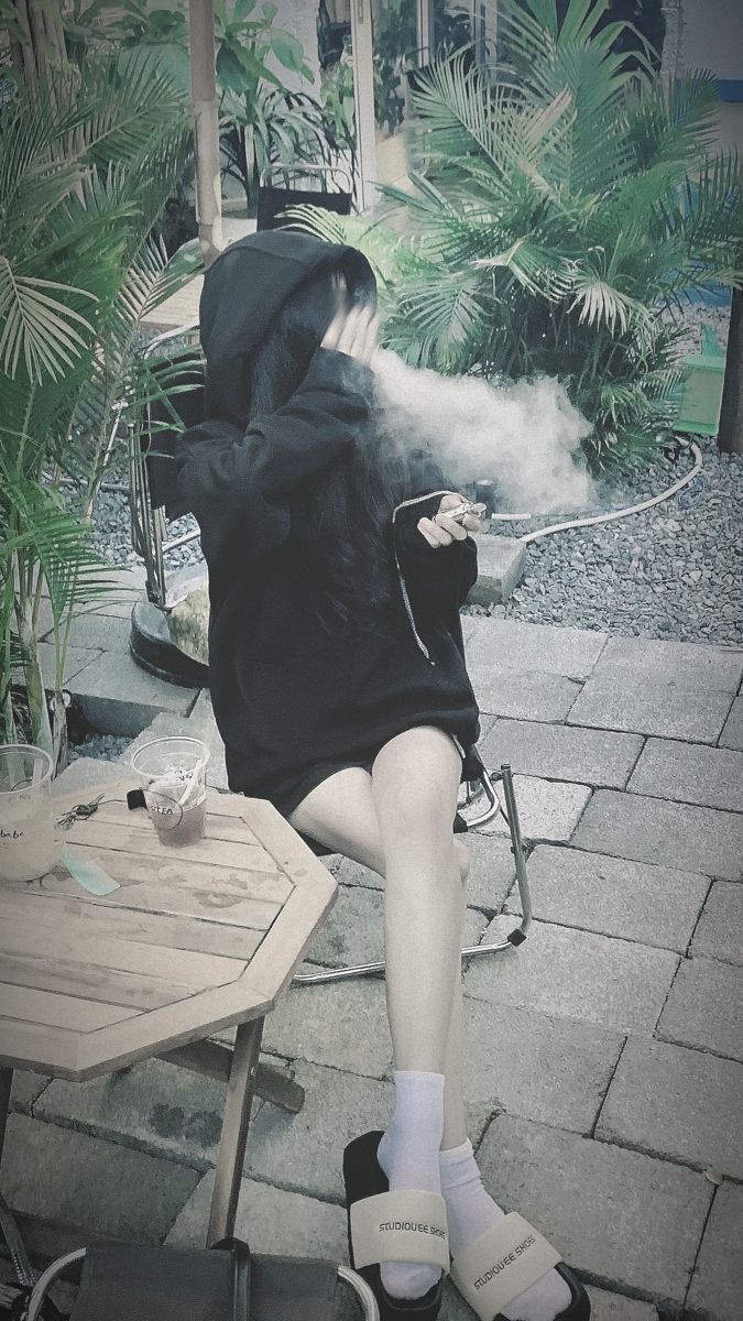 Gái xinh trong áo hoodie đen ngồi trên ghế hút thuốc