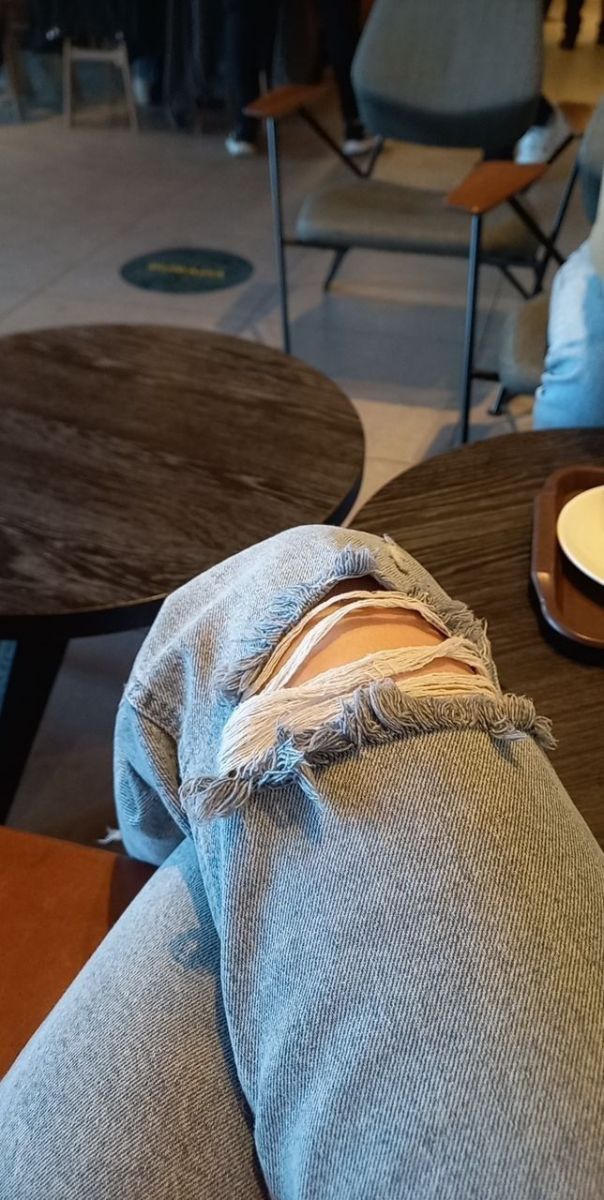 Người đàn ông ngồi thư giãn trong quán cà phê với quần jeans rách
