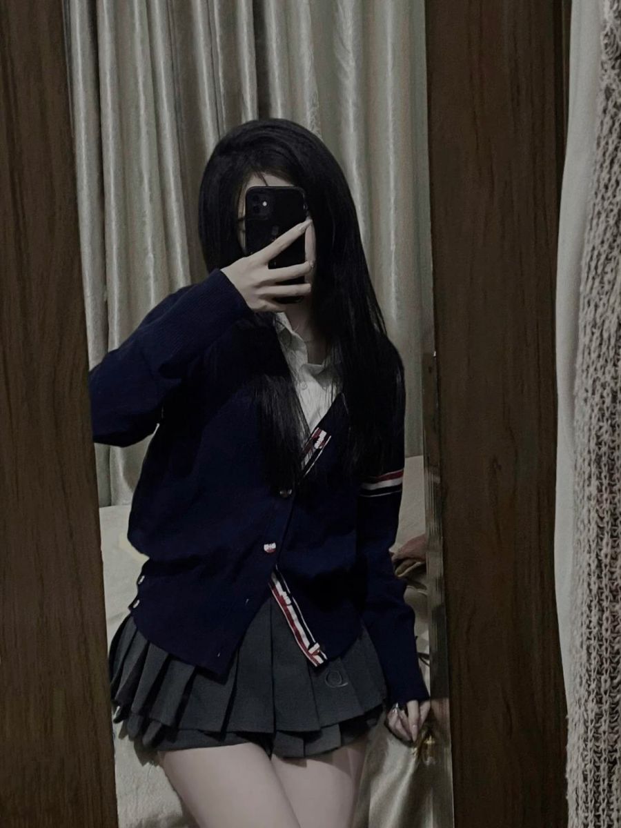 Nữ mặc áo cardigan màu tối và chân váy xếp ly tạo dáng trong gương