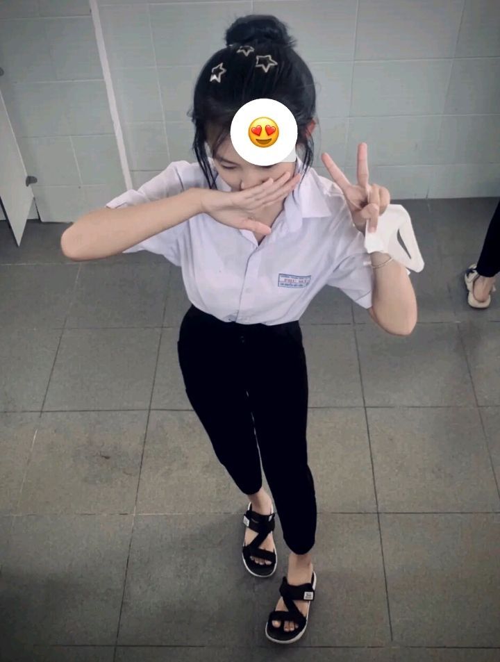 Nữ sinh mặc đồng phục áo sơ mi trắng và quần đen tạo dáng với tay làm đầu V