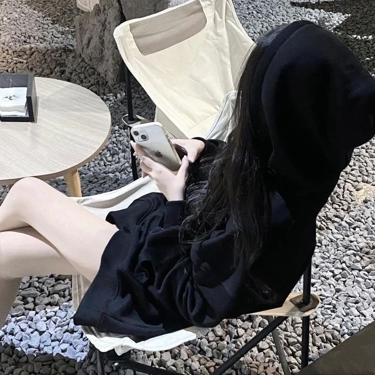Ảnh gái trẻ mặc áo hoodie đen ngồi trên ghế nhựa