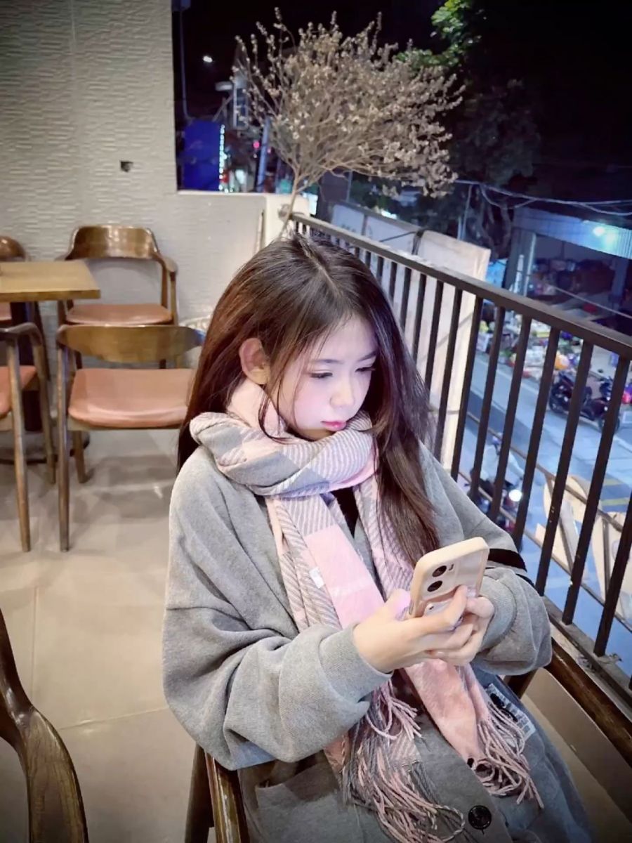 Ảnh gái trẻ mặc áo khoác xám quàng khăn hồng trong quán cà phê