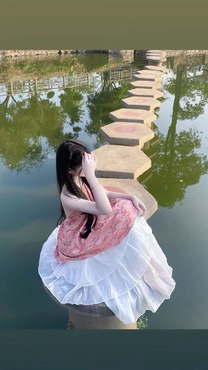 Ảnh gái xinh mặc váy hồng trắng ngồi bên hồ nước