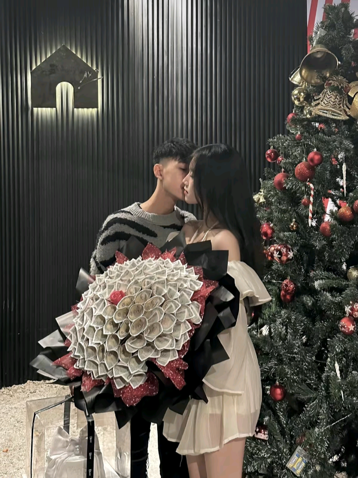 Cặp đôi mặc áo len sọc trắng đen và váy trắng bên cây thông Giáng Sinh