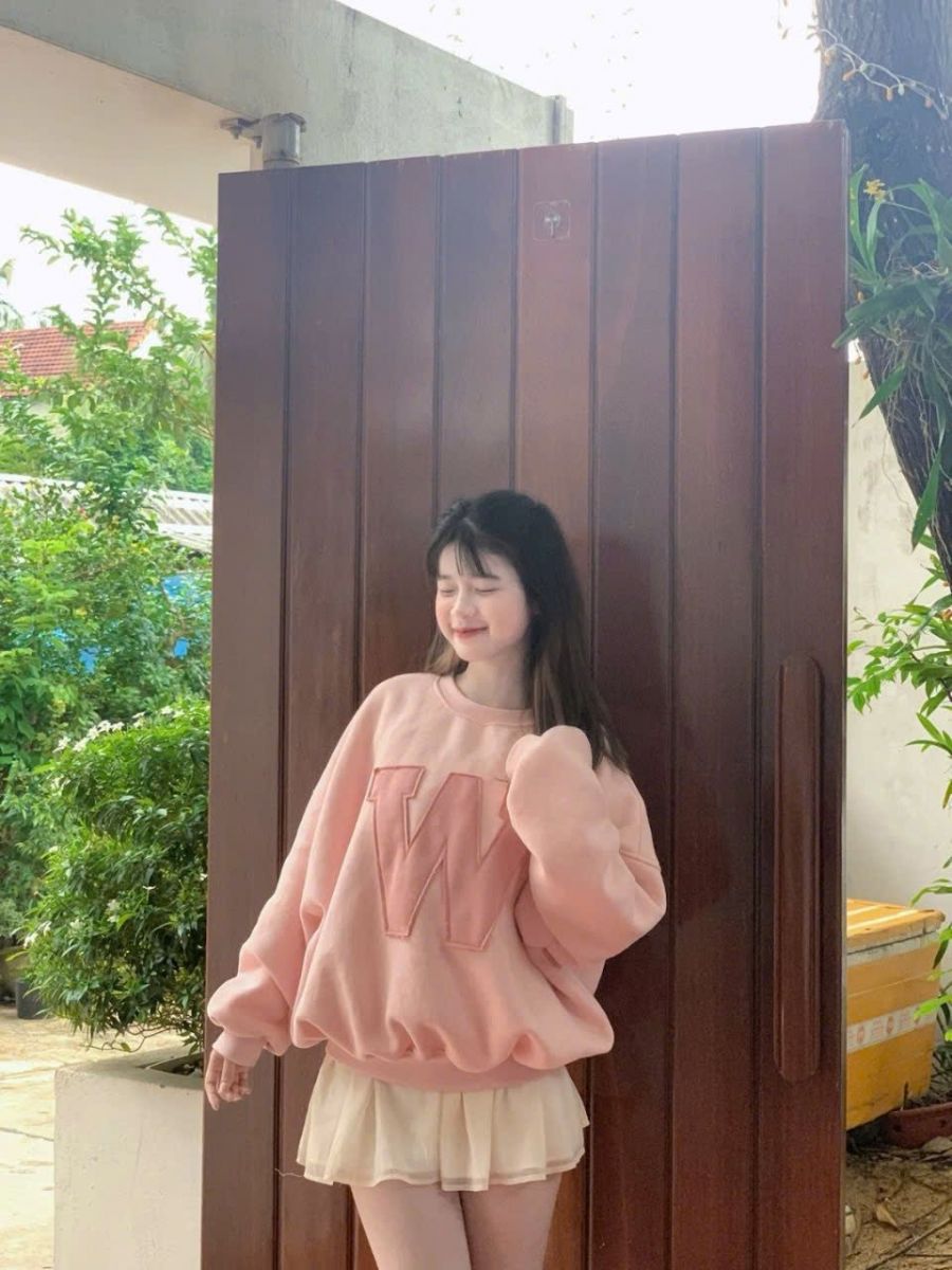 Cô gái đẹp mặc váy trắng và áo sweater hồng bên cửa gỗ