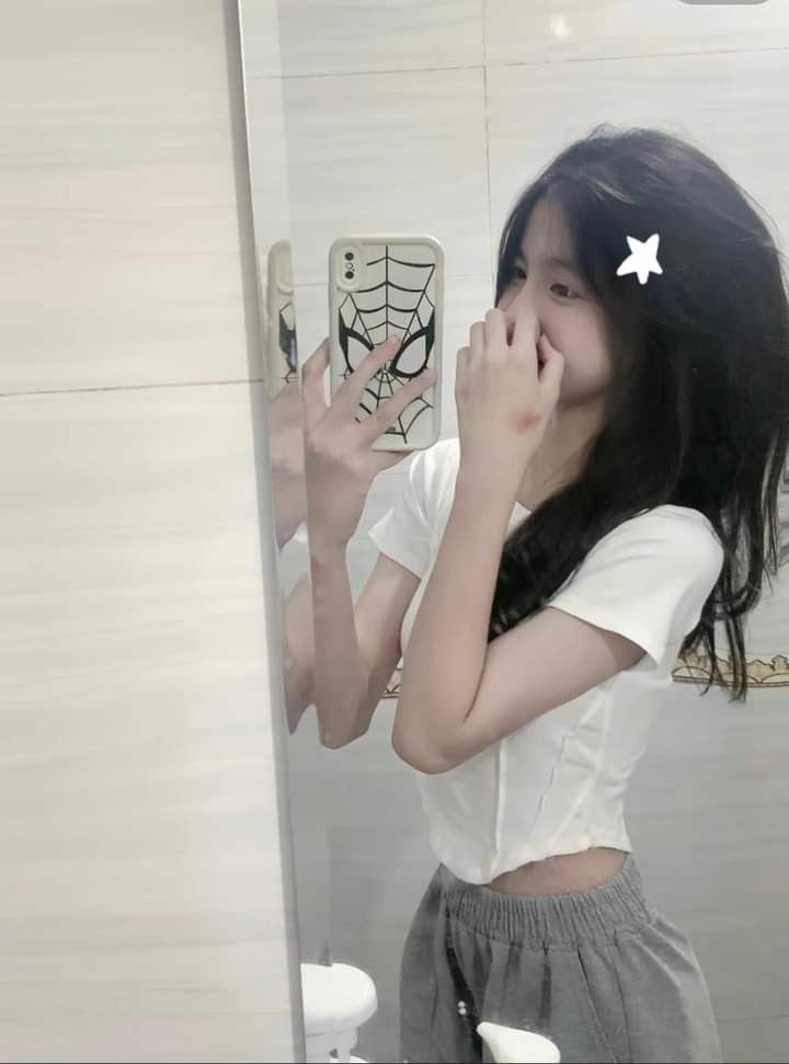Cô gái mặc áo phông trắng và quần đùi xám chụp ảnh trong gương