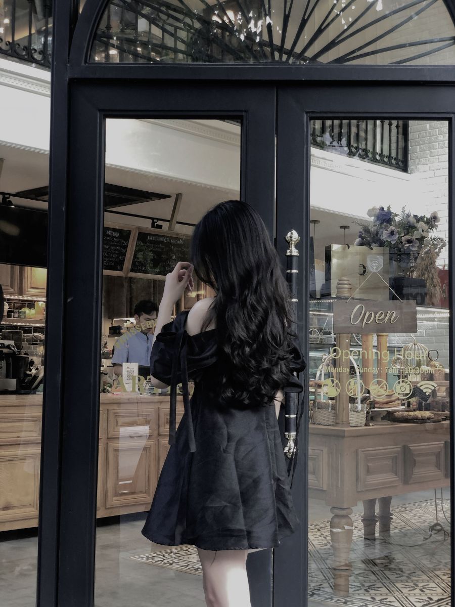 Cô gái mặc váy đen bên cửa kính quán cà phê