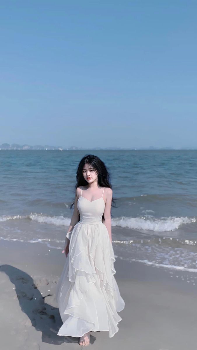 Cô gái mặc váy trắng đi bộ trên bãi biển