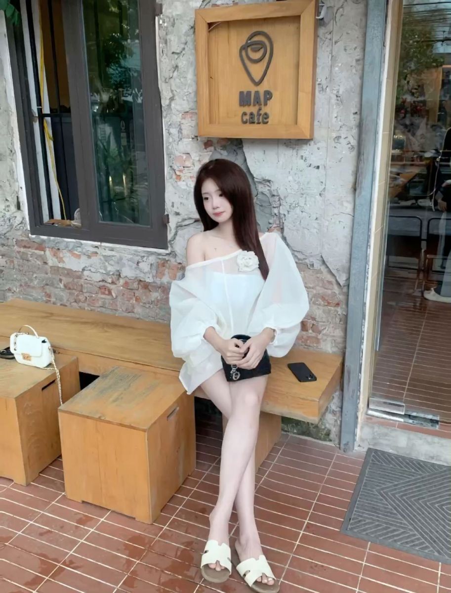Cô gái trẻ mặc áo blouse trắng và quần short đen tại quán cà phê