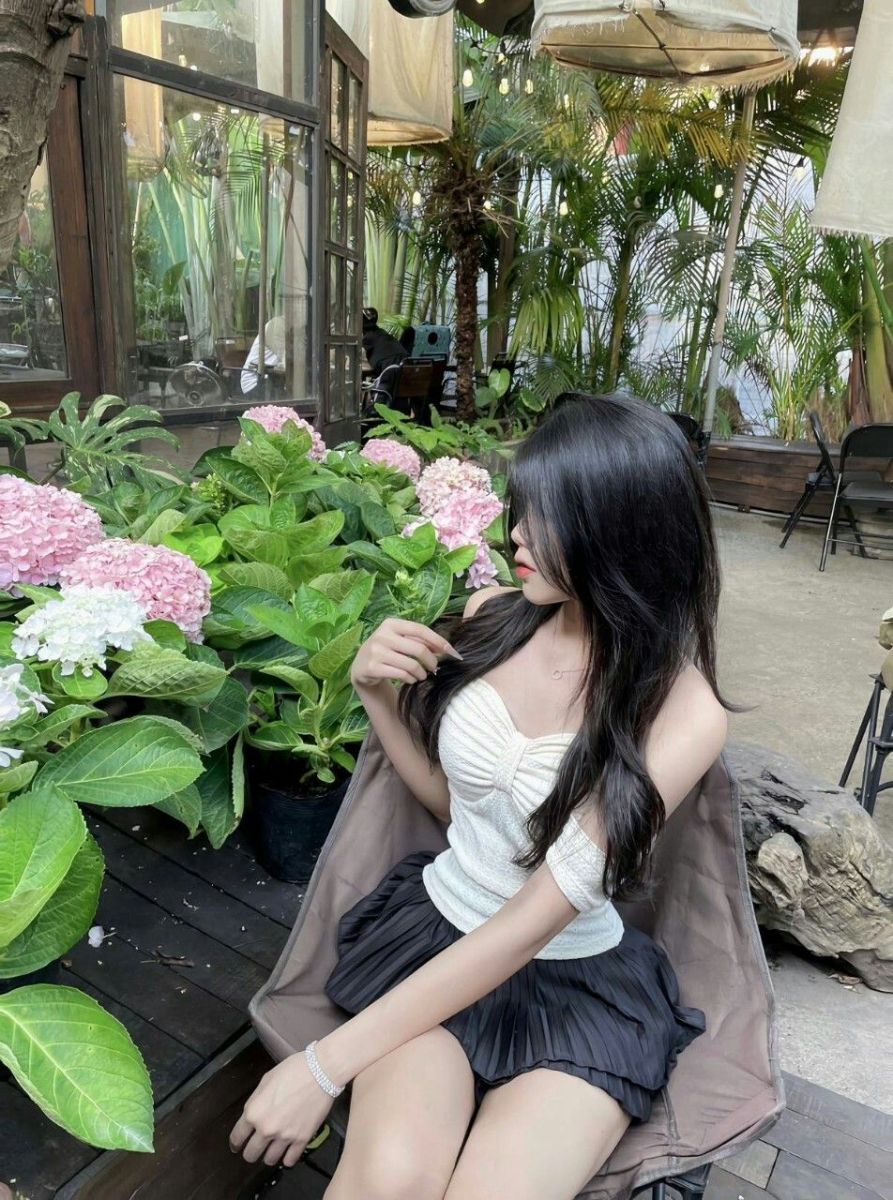 Cô gái trẻ mặc áo croptop trắng và chân váy đen ngồi thư giãn trong quán cà phê