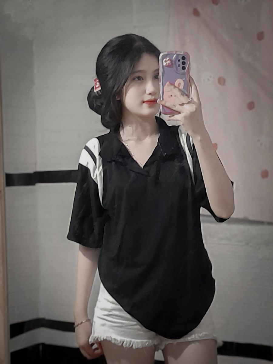 Cô gái trẻ mặc áo phông đen và quần short trắng tạo dáng chụp hình selfie