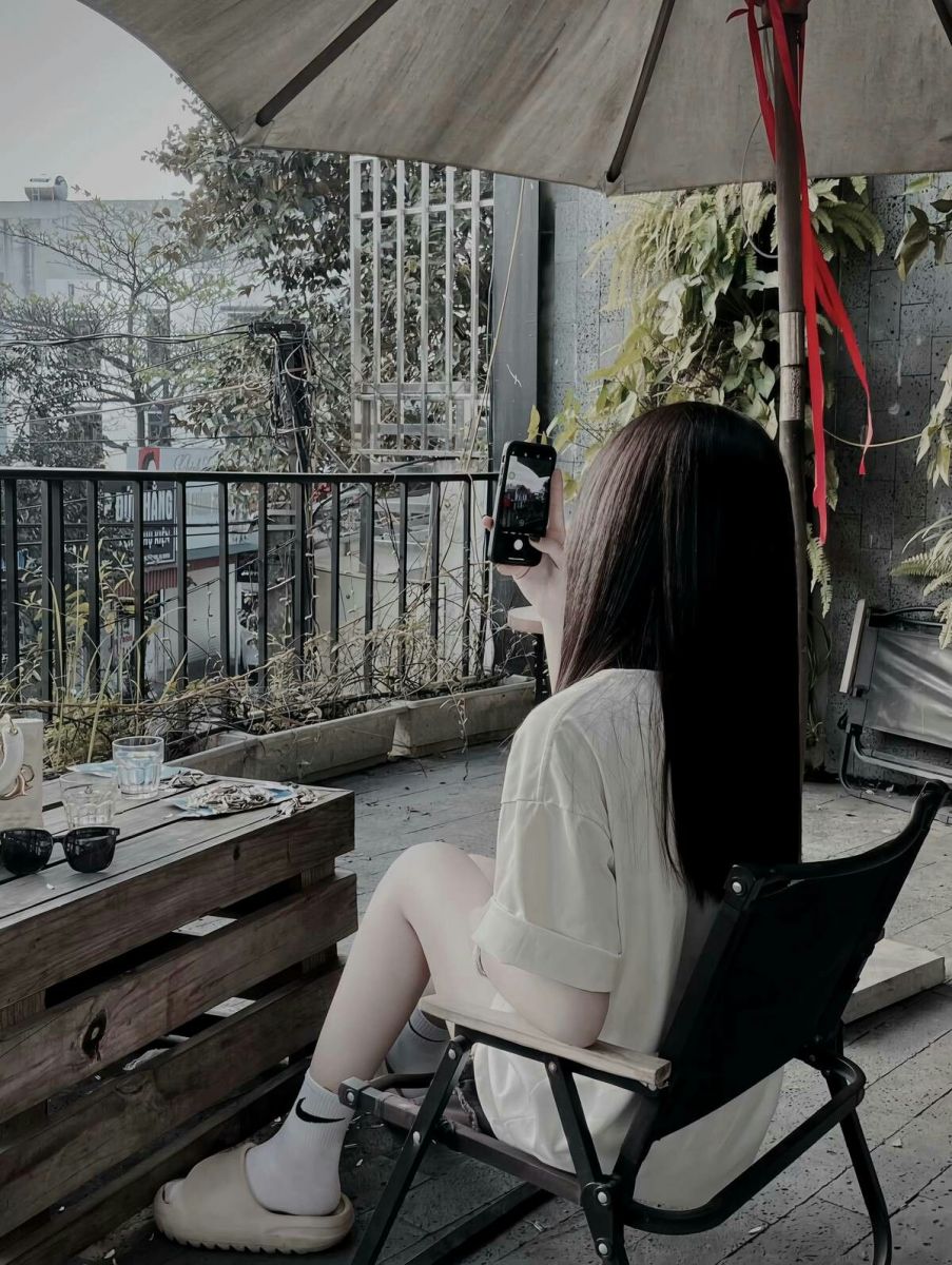 Cô gái trẻ xinh đẹp ngồi trên ghế xếp chụp ảnh ngoài trời