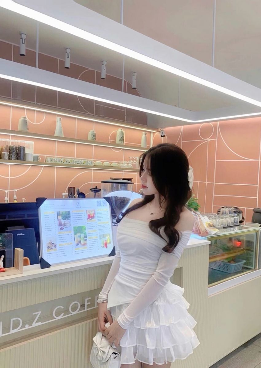 Cô gái trẻ xinh đẹp trong váy trắng tại quán cafe hiện đại
