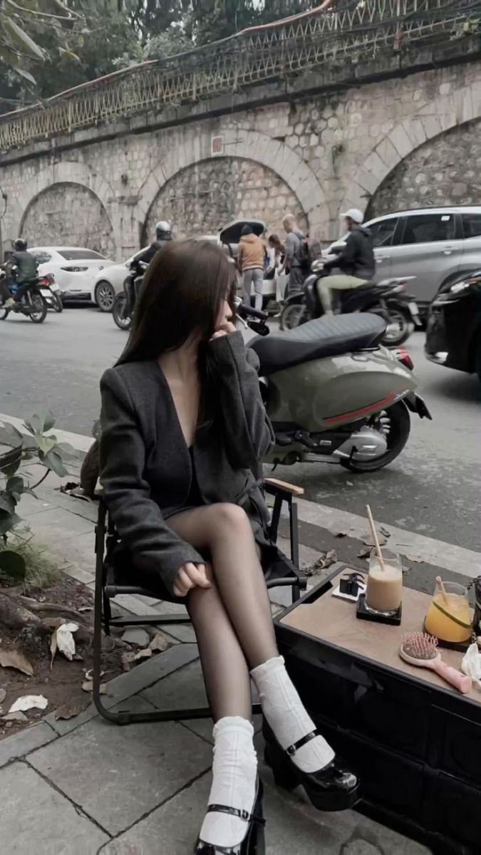 Cô gái xinh mặc áo khoác đen ngồi trên ghế xếp bên đường