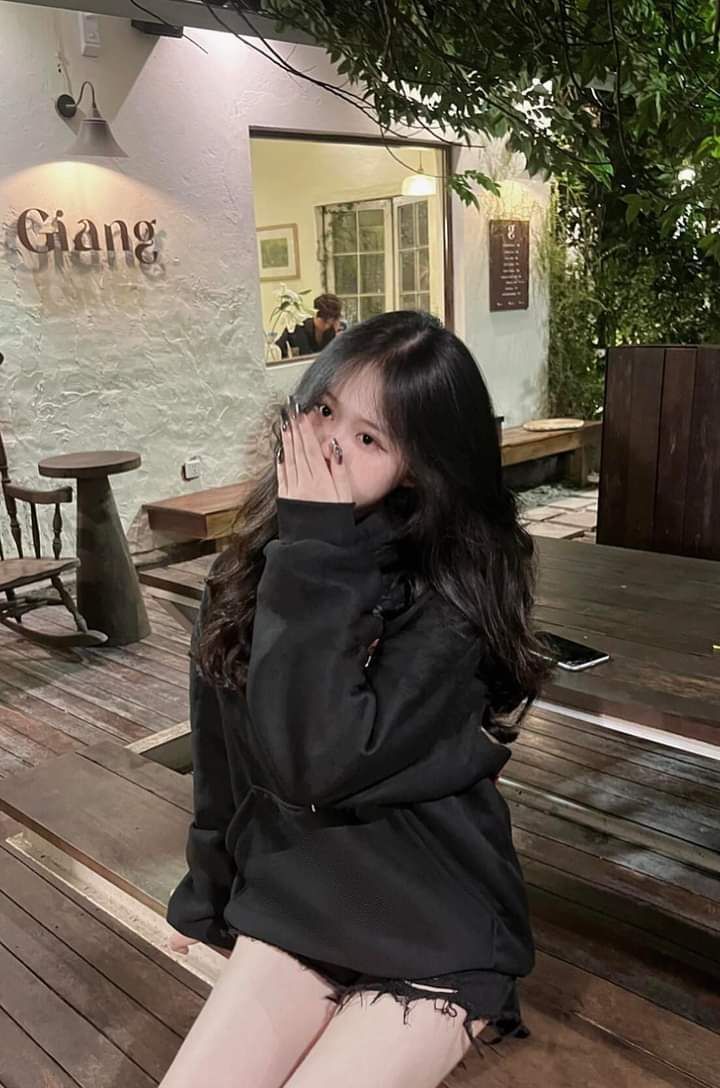 Gái che mặt trong hoodie đen tại quán cà phê ấm cúng
