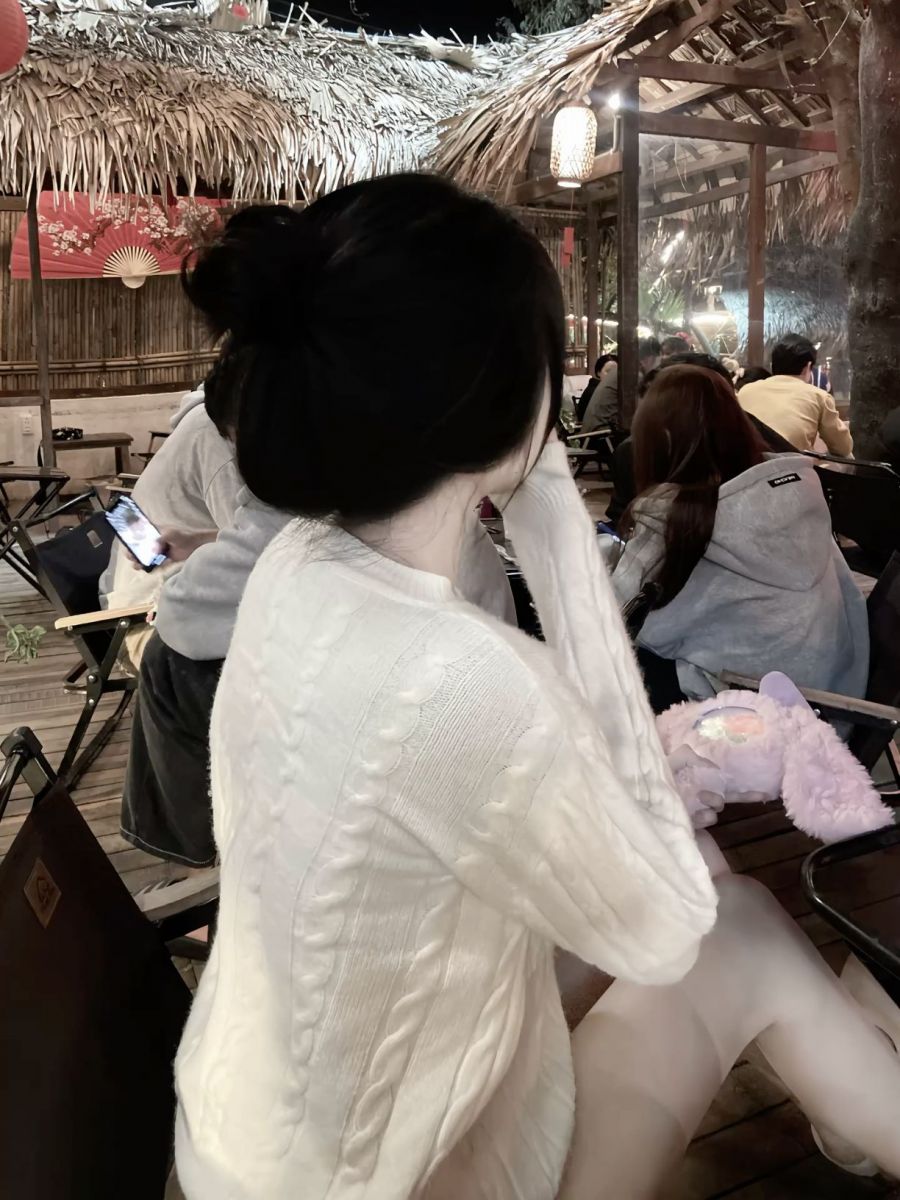 Gái xinh mặc áo len trắng ngồi cúi đầu sử dụng điện thoại