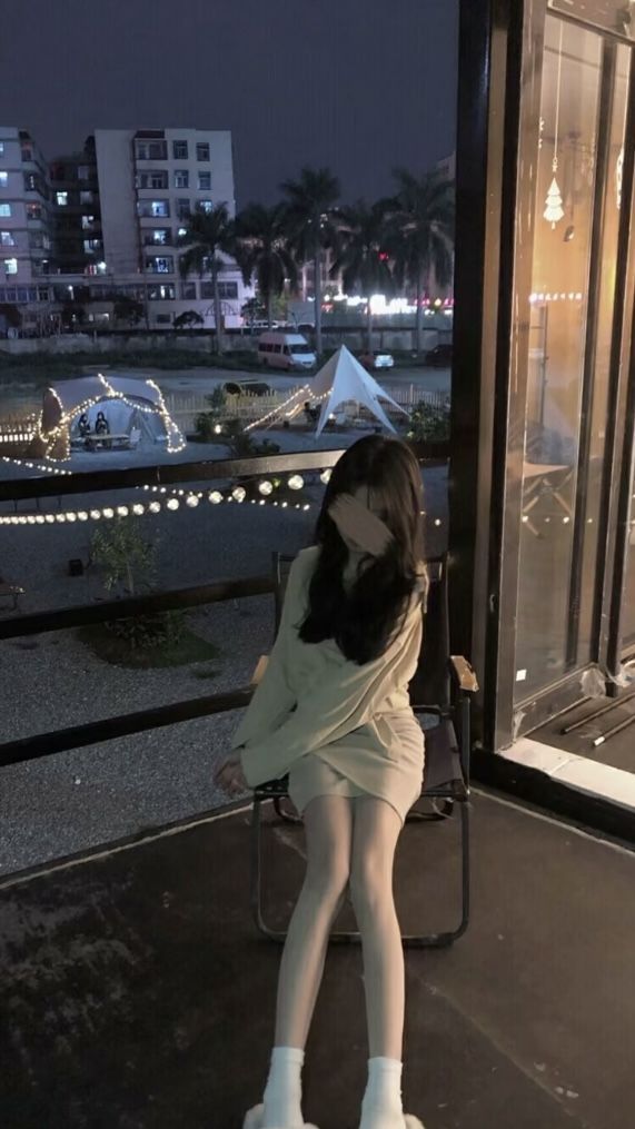 Gái xinh mặc áo phông rộng và tất trắng ngồi trên ghế buổi tối tại quán cà phê