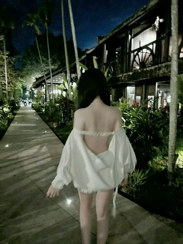 Gái xinh mặc áo sơ mi trắng đi bộ trong khu vườn rợp bóng cây