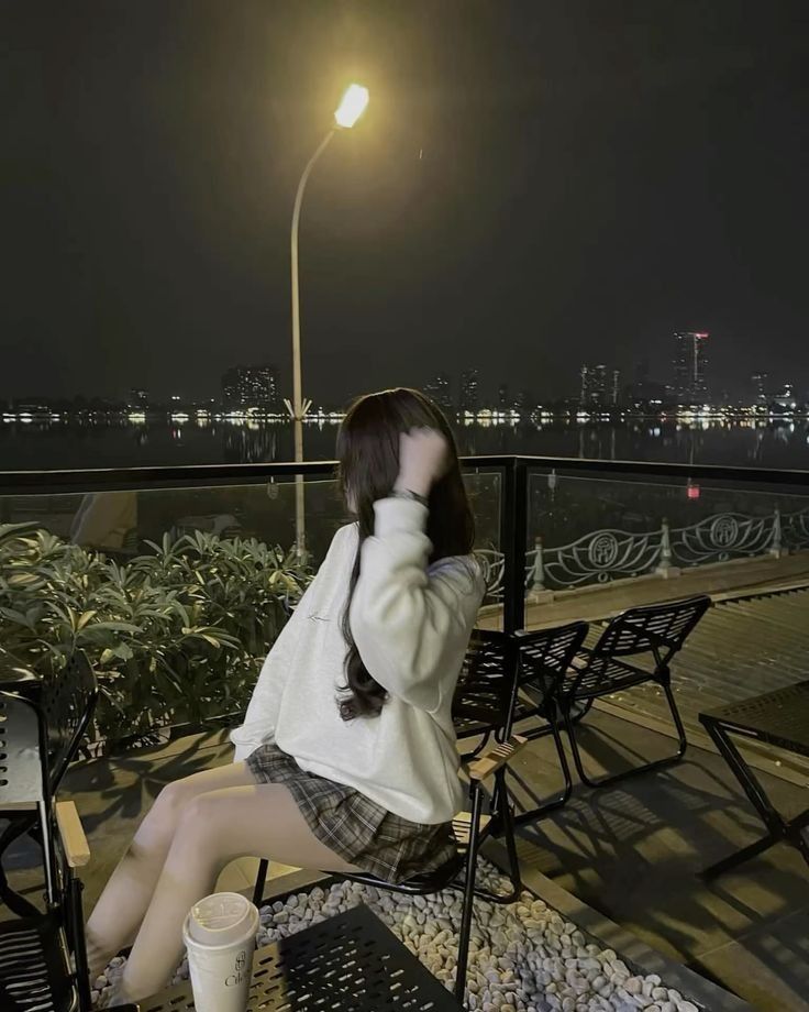 Gái xinh ngồi trên ghế mặc áo sweater trắng và chân váy kẻ dáng vượt tông ở quán cà phê bên bờ sông