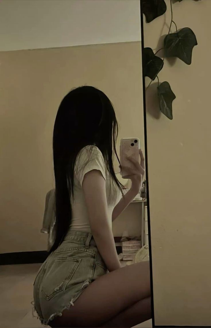 Ảnh gái trẻ mặc áo thun trắng và quần shorts jeans chụp selfie trong gương