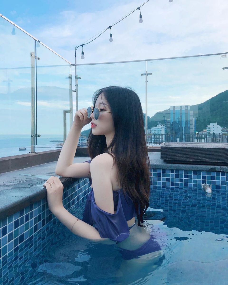 Cô gái mặc bikini và áo croptop màu tím ngồi bên hồ bơi
