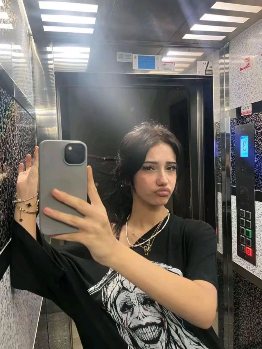 Cô gái trẻ mặc áo phông oversized chụp selfie hài hước trong thang máy