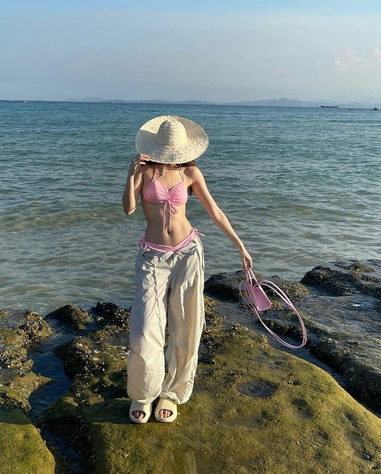 Cô gái trẻ mặc bikini hồng và quần dài bên bờ biển