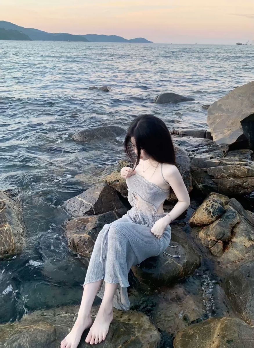 Gái đẹp mặc váy xám ôm sát ngồi trên đá ven biển