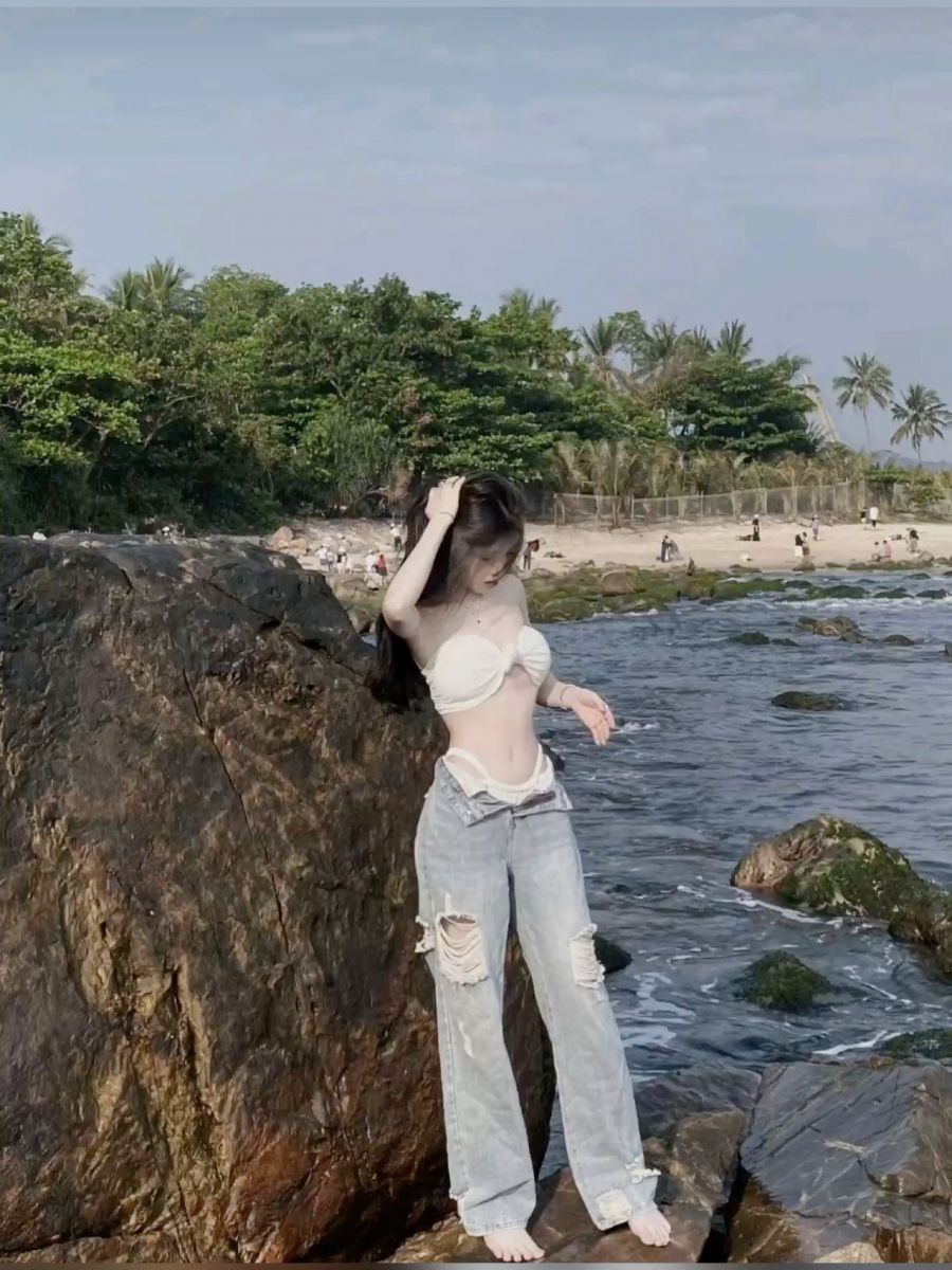 Gái xinh mặc áo bikini trắng và quần jeans rách bên bờ biển